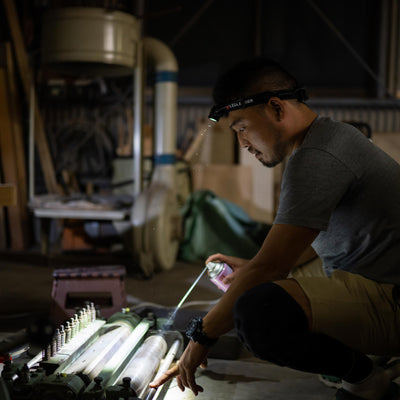 H15R Core Headlamp worn by a man kneeling in a workshop headlamp beam illuminating a machining setup in a dim environment