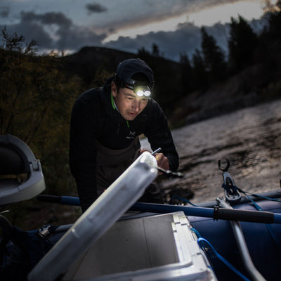 H19R Core Headlamp worn by a person in black outdoors at dusk with dual LEDs lit leaning over gear on a boat