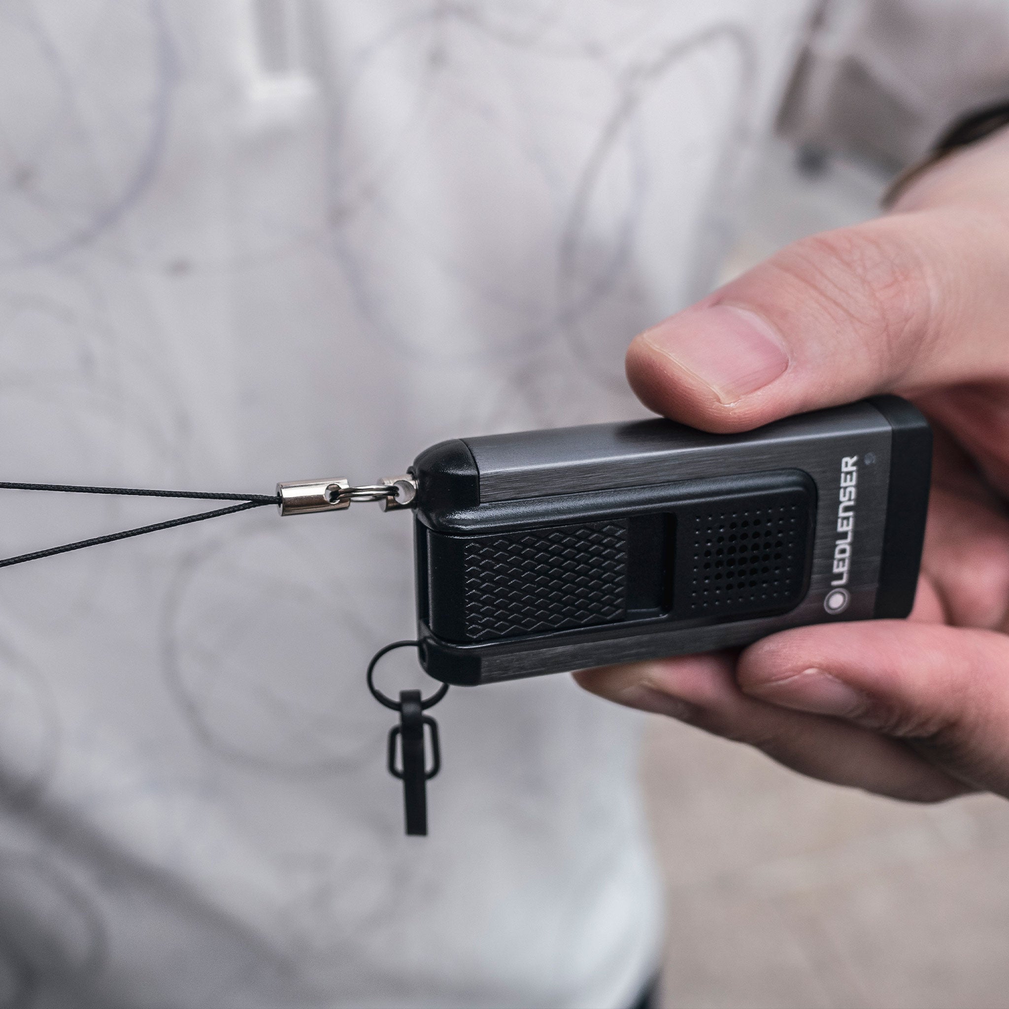 K6R Safety Keychain Light held in hand compact black rechargeable key ring torch with a lanyard; Ledlenser branding visible