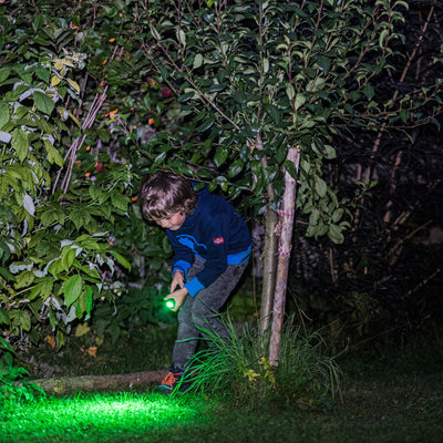 Kidbeam4 Torch being used by a child outdoors at night gripping a green lit torch among grass and bushes
