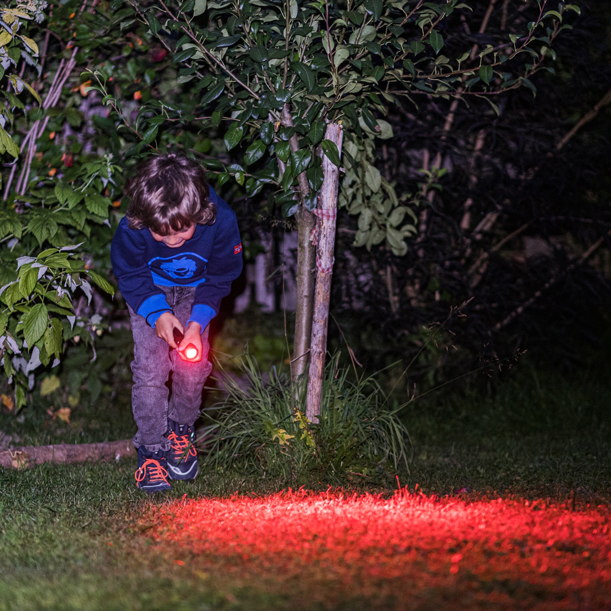 Kidbeam4 Torch held by a child outdoors at night with red light emitting from the compact handheld torch illuminating grass and surrounding foliage