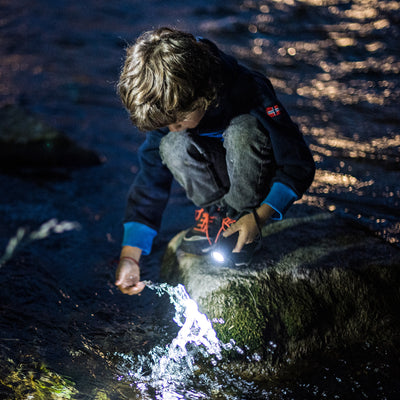 Kidbeam4 Torch in use by child kneeling on rocks beside a stream handheld compact flashlight emitting white light