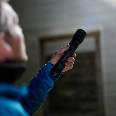 Ledlenser P17R Core Torch held in a hand with a blue sleeve indoors against a dark background