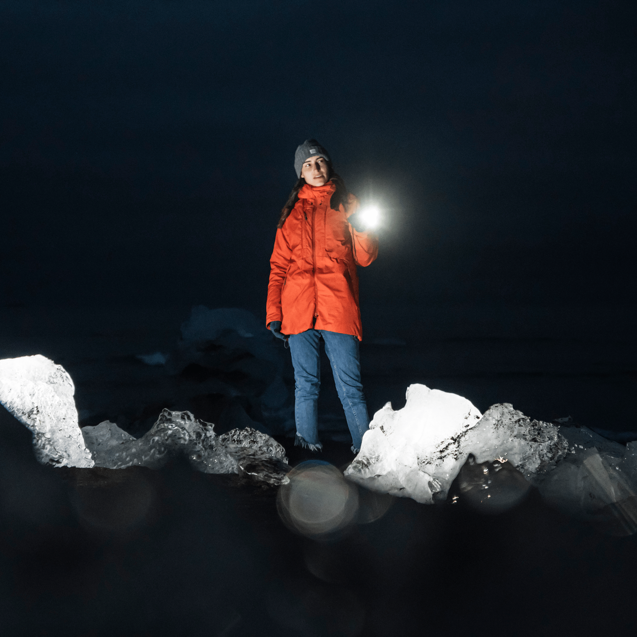 Ledlenser P18R Signature Torch held by a person in an orange jacket at night on rocky terrain