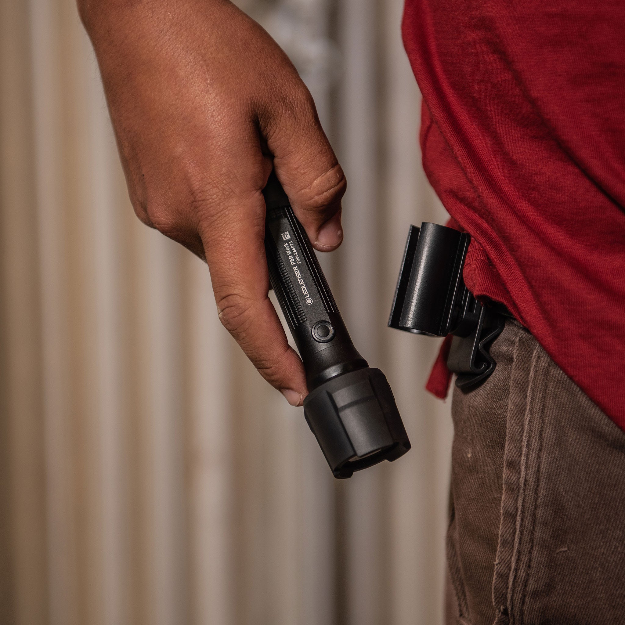 Ledlenser P5R Work Torch held in a right hand compact black flashlight with textured grip and belt holster on the wearer
