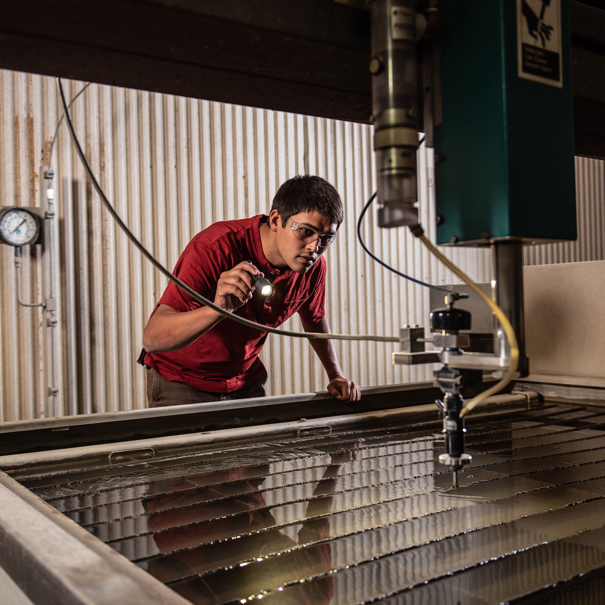 Ledlenser P5R Work Torch being held by a worker in a workshop illuminating a metal workpiece with a compact rechargeable handheld light