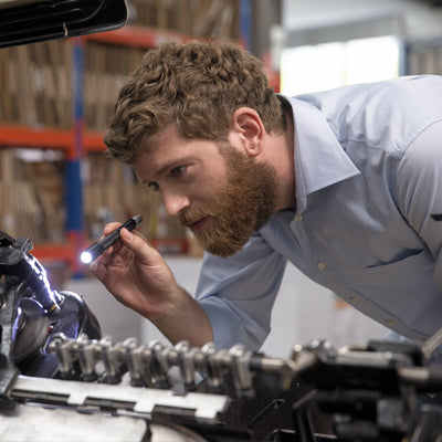 Ledlenser i6R Rechargeable Pen Light held by a technician inspecting mechanical components in a workshop
