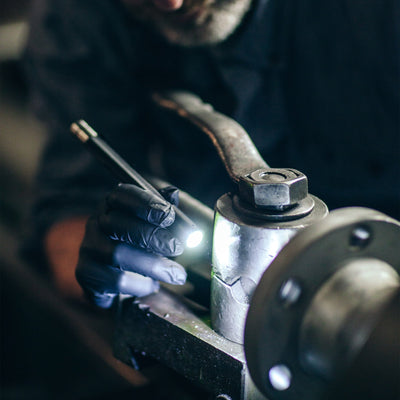 Ledlenser i6 Battery Operated Pen Light held by gloved hand near a bolt on industrial machinery illuminating the workspace
