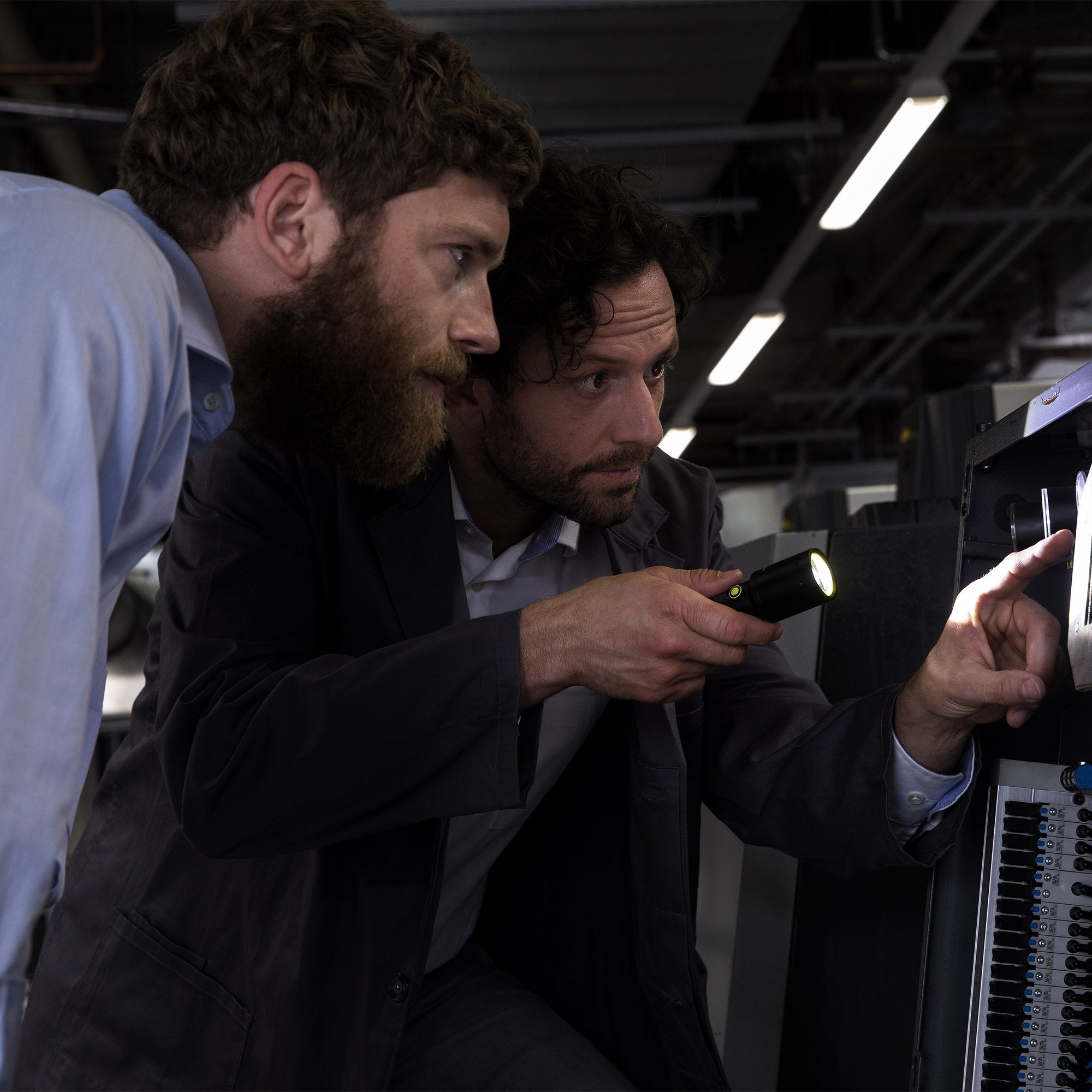 i7 Torch being used by two professionals inspecting a rack mounted control panel in a dim workshop