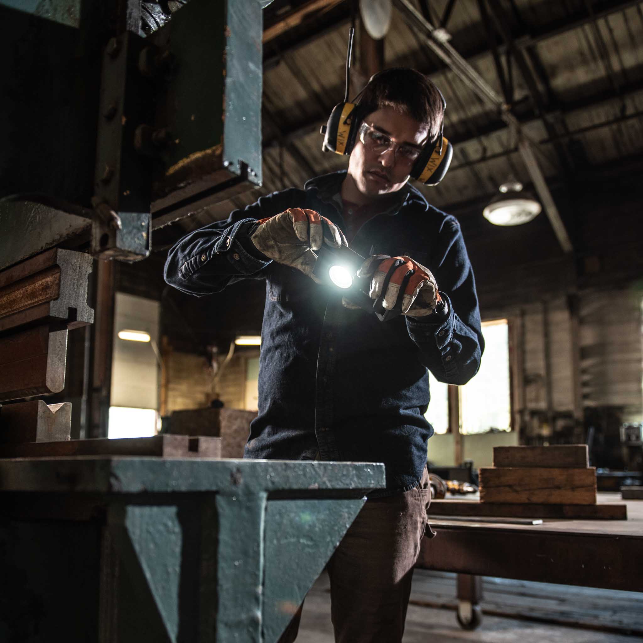Ledlenser iF3R Spotlight held by a worker in a workshop wearing gloves and safety goggles with earmuffs