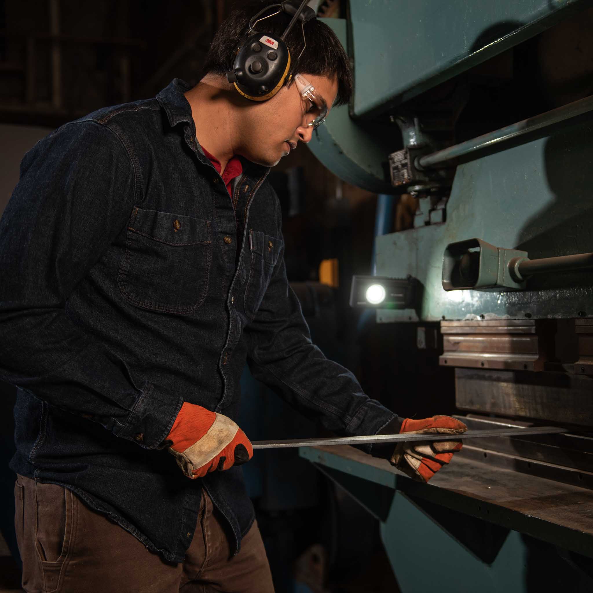 iF3R Spotlight shown in a busy industrial workshop with a technician wearing safety glasses and earmuffs inspecting metal on a machine handheld light visible
