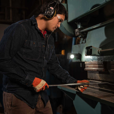 iF3R Spotlight shown in a busy industrial workshop with a technician wearing safety glasses and earmuffs inspecting metal on a machine handheld light visible