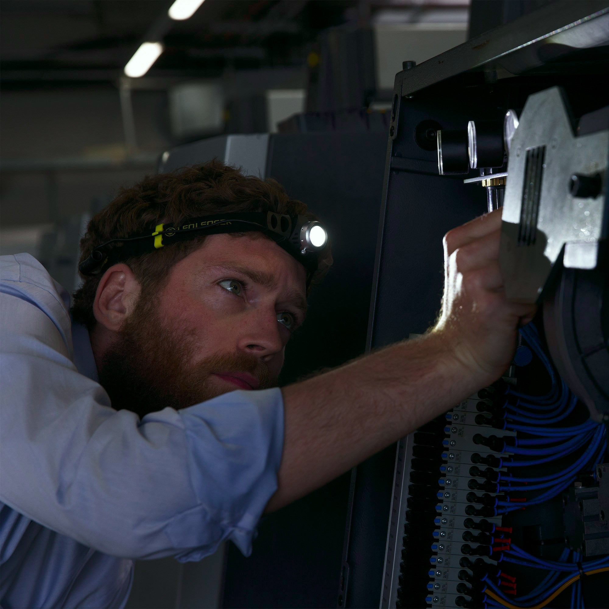 iH3 Battery Operated Headlamp worn by a technician inspecting an electrical control panel in a workshop