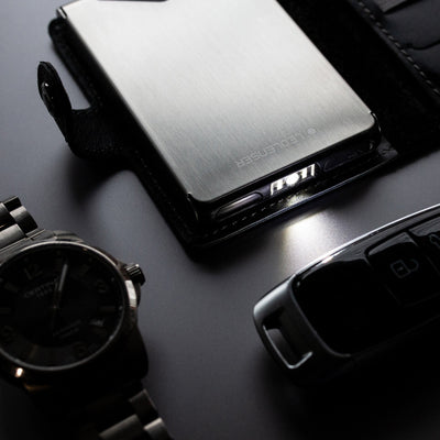 Ledlenser Lite Wallet® metal compact wallet with brushed aluminum finish closed with a small edge light visible shown beside a wristwatch and car key fob