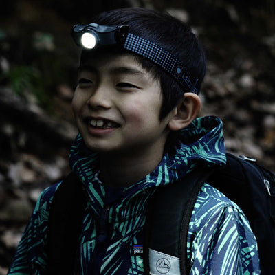 MH3 Headlamp worn by a young hiker with the light on adjustable dotted strap outdoors in a forest setting