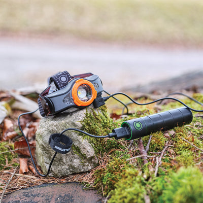 Flex3 Powerbank with headlamp attachment orange front ring and black cylindrical body on a mossy rock with a charging cable