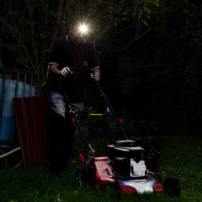 Ledlenser MH4 Powercase Combo headlamp with charging case worn by a person outdoors at dusk beam shining ahead near a lawn mower