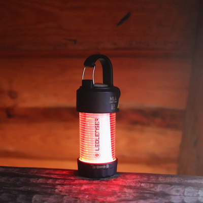 ML4 Lantern: black cylindrical lantern with red glow hanging handle on top Ledlenser branding on the body resting on a wooden surface