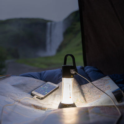 Ledlenser ML6 Lantern standing upright inside a tent on a map lantern lit with a charging cable connected to a smartphone