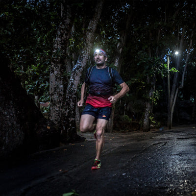 NEO4 Battery Operated Headlamp worn by a man running at night on a damp forest path with trees; headlamp lit