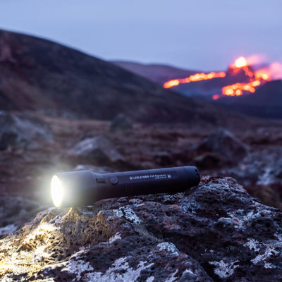 P6R Signature Torch resting on rocks outdoors with the front beam illuminated; a black cylindrical Ledlenser torch in a rugged outdoor setting