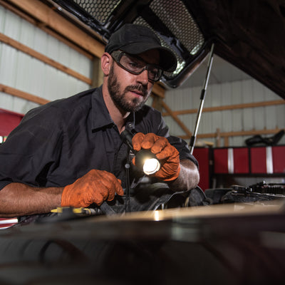 Ledlenser P7R Work Torch held by mechanic wearing cap and safety glasses inspecting a vehicle engine bay in a workshop