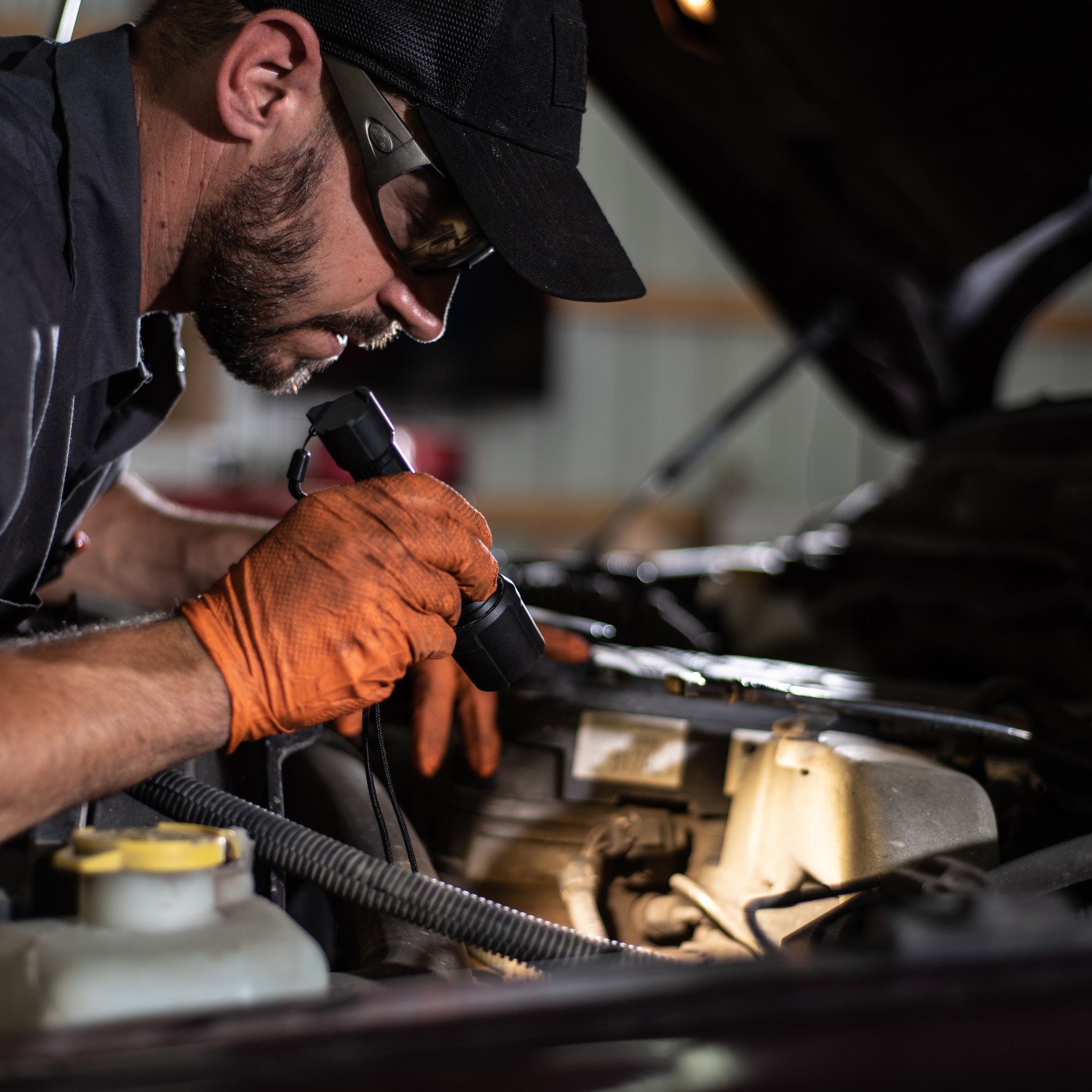 P7R Work Torch used by a technician with cap and orange gloves inspecting a car engine in a workshop