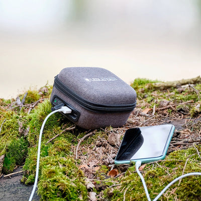 MH4 Powercase Combo Headlamp & Charging Case in grey fabric case with USB cable connected outdoors on moss near a smartphone