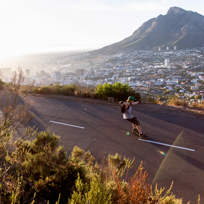 XEO19R Rechargeable Headlamp on a person skateboarding down a hillside road with city and mountain backdrop