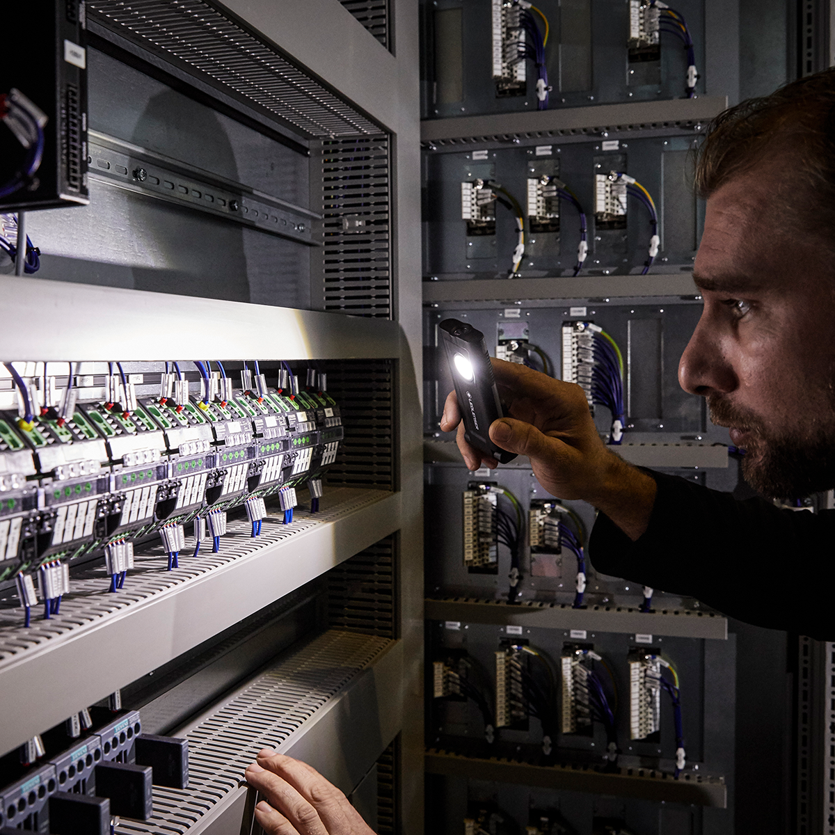 Ledlenser iF2R Spotlight handheld flashlight being tested near an electrical control panel with wiring and terminal blocks