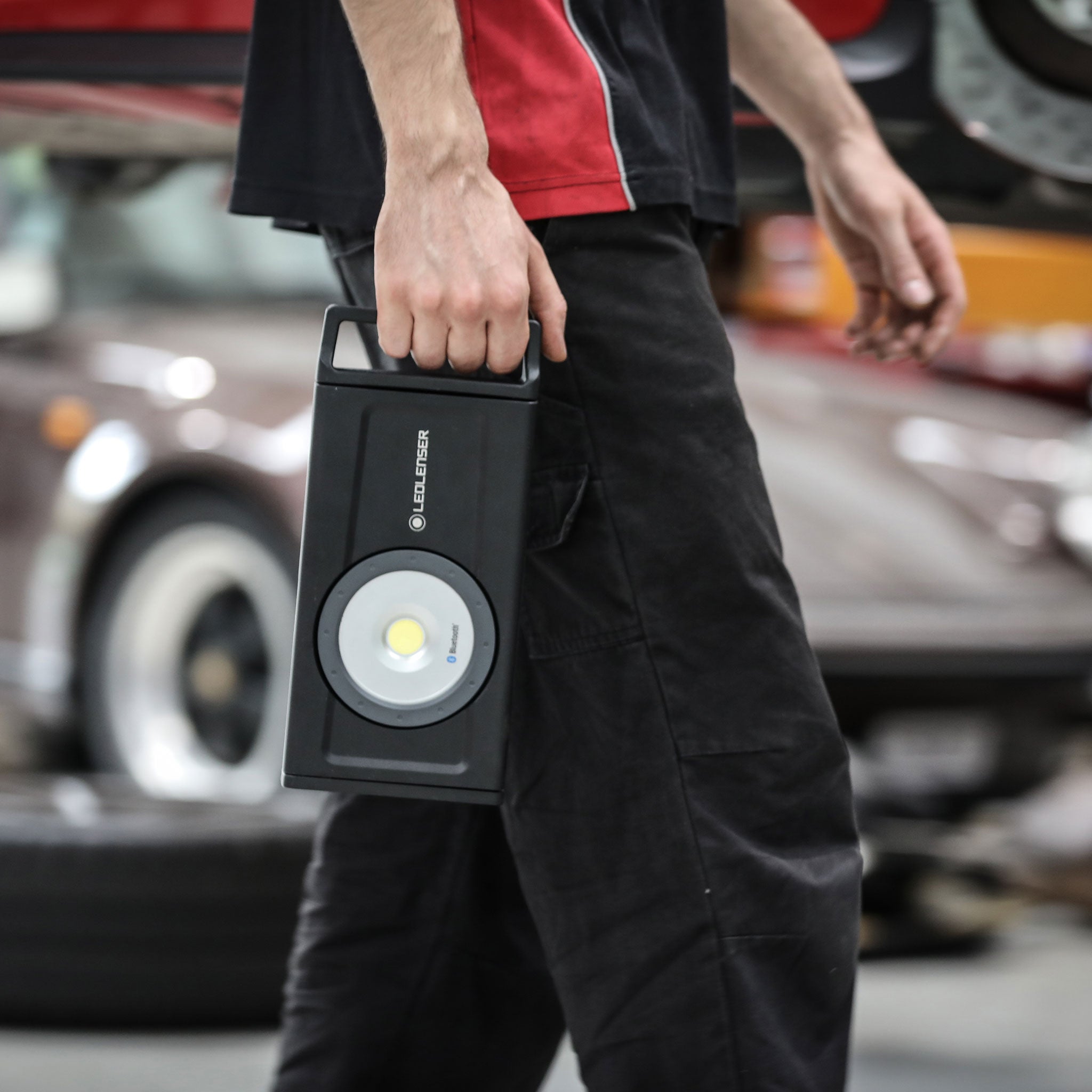 Ledlenser iF8R Spotlight handheld work light with a circular LED module in a black rectangular body carried by a user in a workshop