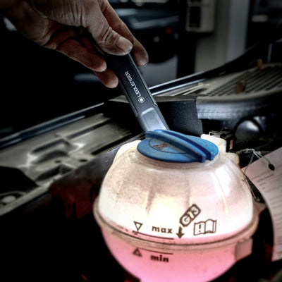 Ledlenser iW4R Work Light being held near a car engine bay with a blue coolant reservoir cap visible